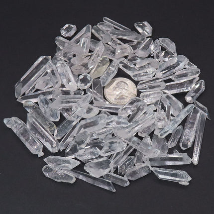 100 Arkansas A Grade Quartz Crystal Double Terminated Points with a quarter coin for scale on a dark background