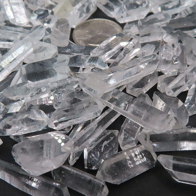 Close up of 100 Arkansas A Grade Quartz Crystal Double Terminated Points with a quarter coin for scale on a dark background