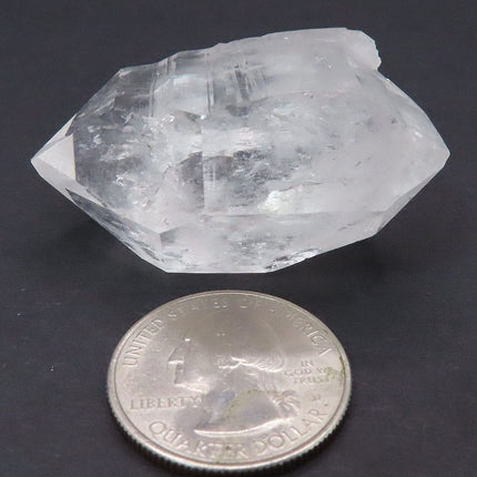 Arkansas Quartz Crystal Double Terminated Point next to a quarter for scale on a dark background