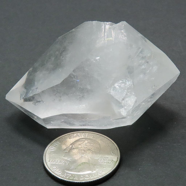 Arkansas Quartz Crystal Double Terminated Point next to a quarter for scale on a grey background