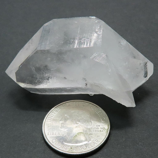 Arkansas Quartz Crystal Double Terminated Point next to a quarter for scale on a grey background