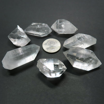 5 Arkansas Arkimer Quartz Crystal Double Terminated Points & 2 DT/ET next to a quarter for scale on a grey background