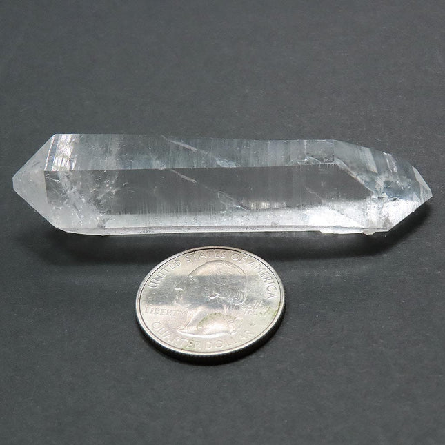 Arkansas Quartz Crystal Double Terminated Point next to a quarter for scale on a grey background