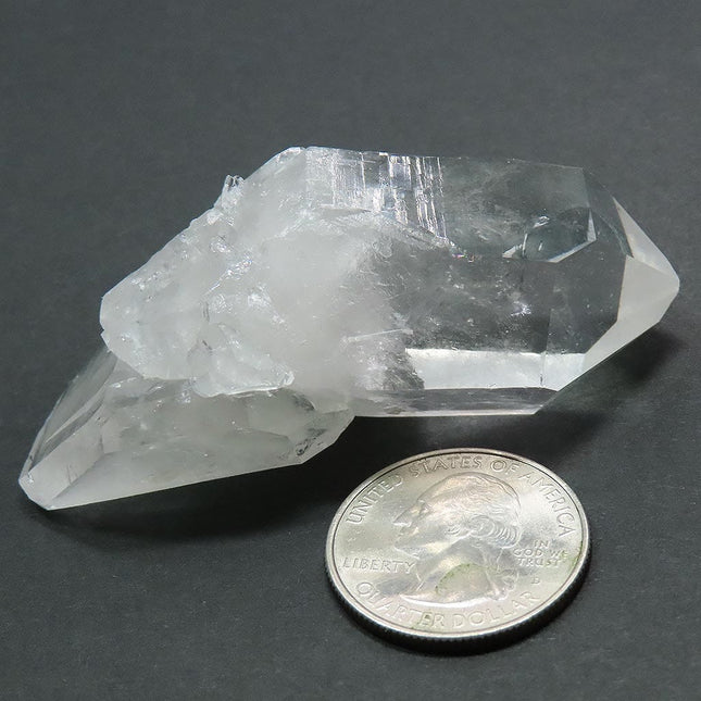 Arkansas Quartz Crystal Double Terminated Point next to a quarter for scale on a grey background