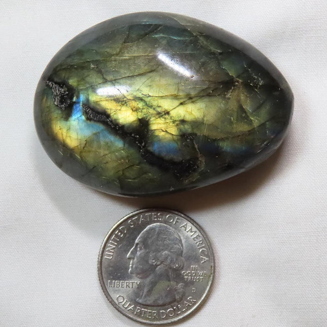 Polished Labradorite Palm Stone from Madagascar next to a U.S. quarter dollar for scale on a white background