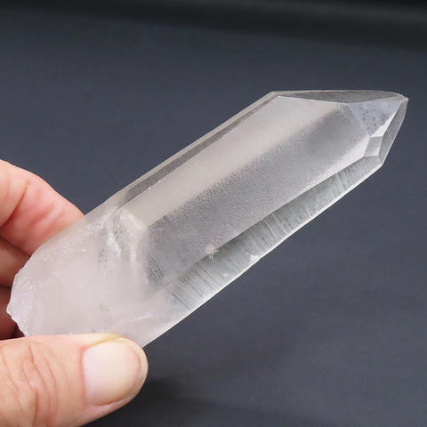 Clear Lemurian Seed Quartz Crystal Point with Window from Brazil held by a hand against a dark background