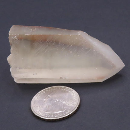 Pink Lemurian Seed Quartz Crystal Point from Brazil next to a U.S. quarter on a dark background