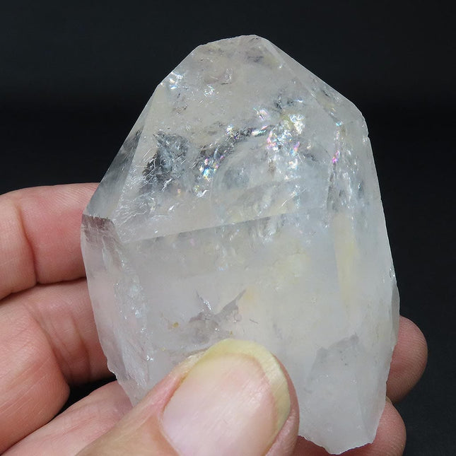 Arkansas Quartz Crystal Etched Point with Rainbow & Self-Healed Base being held by fingers on a dark background