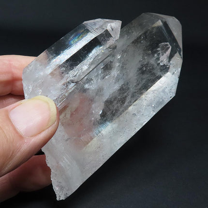 Arkansas Quartz Crystal Tabby Point with Rainbow held by a hand against a dark background