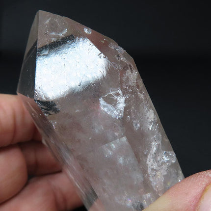 Ding on an Arkansas Quartz Crystal Tabby Point held by a hand against a dark background
