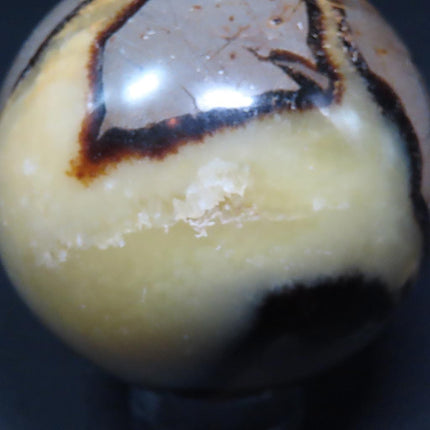 Polished Septarian Nodule Sphere Ball from Madagascar on a stand with a quarter for scale against a dark background