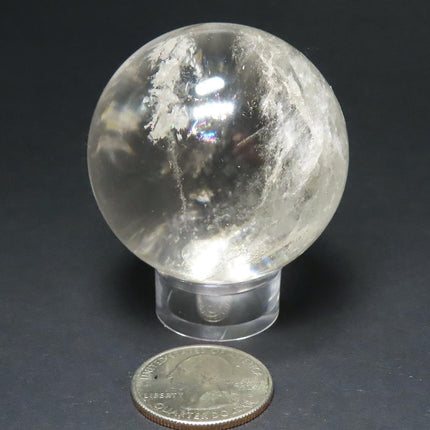 Polished Quartz Crystal Sphere Ball from Brazil with Rainbows on a stand with a US quarter for scale against a dark background