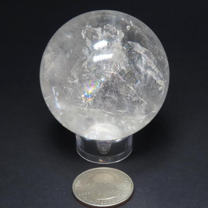 Polished Quartz Crystal Sphere Ball from Brazil with Rainbows on a stand with a US quarter for scale against a black background