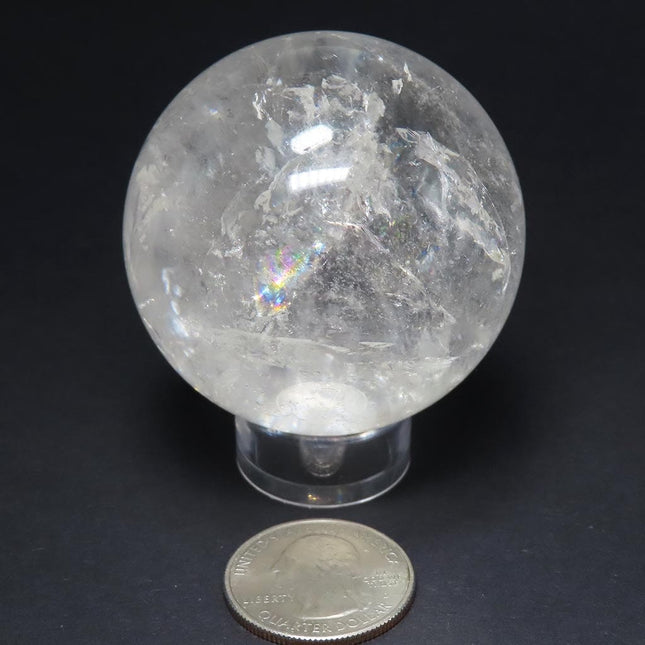 Polished Quartz Crystal Sphere Ball from Brazil with Rainbows on a stand with a US quarter for scale against a black background