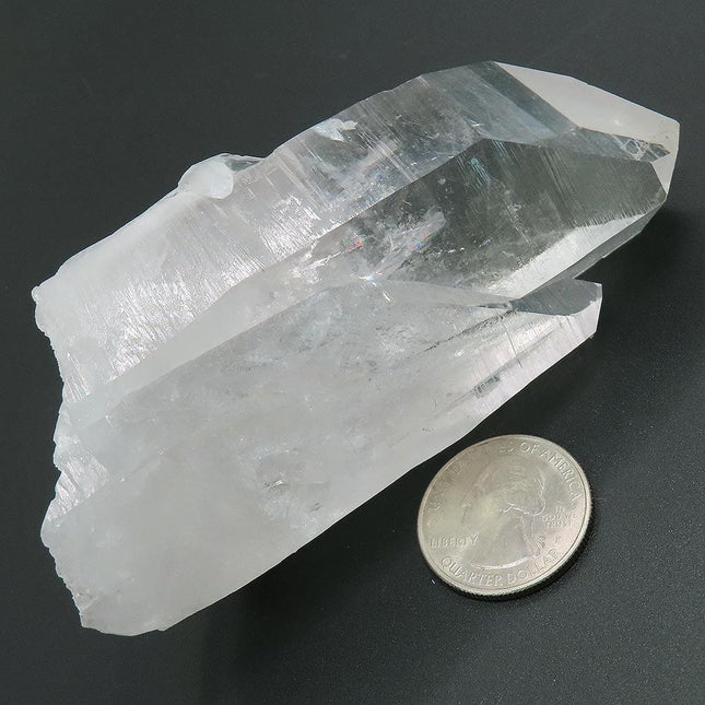 Arkansas Quartz Crystal Point with a Tiny Rainbow next to a U.S. quarter for scale on a dark background