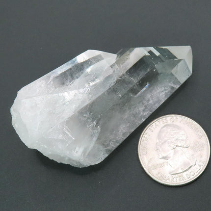 Arkansas Quartz Crystal Point next to a US quarter for scale on a dark gray background