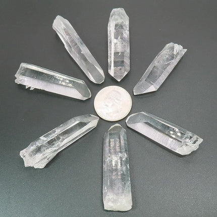 7 Arkansas Quartz Crystal Points arranged in a circle with a US quarter for scale on a gray background
