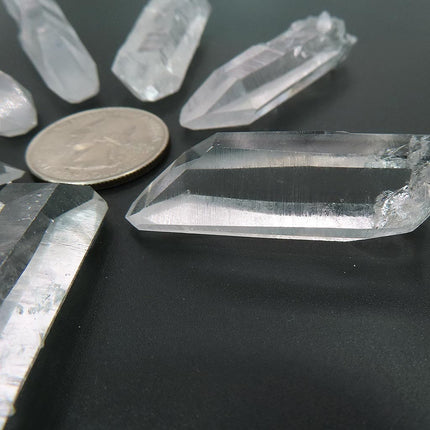 Arkansas clear crystal points on a dark surface with a US quarter for scale