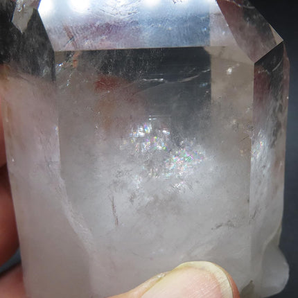 Close-up of Arkansas clear crystal point with rainbow held by a hand against a dark background