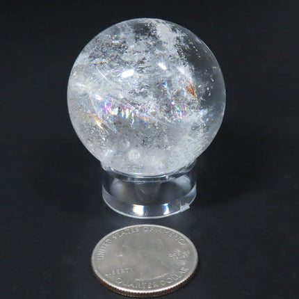 Clear crystal ball from Brazil on a stand with a quarter for scale against a black background