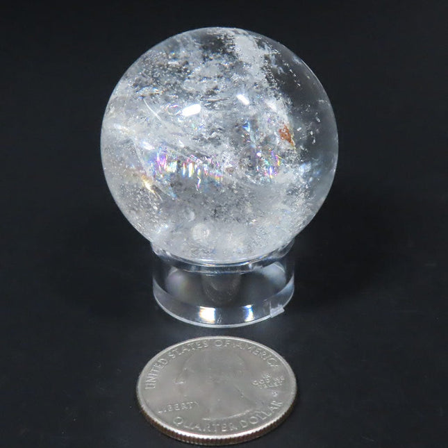 Clear crystal ball from Brazil on a stand with a quarter for scale against a black background