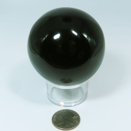 Polished Black Obsidian Sphere Ball from Mexico on a stand with a quarter for scale on a light gray background