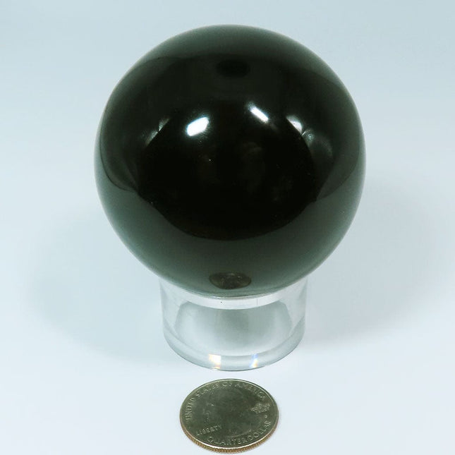 Polished Black Obsidian Sphere Ball from Mexico on a stand with a quarter for scale on a light gray background