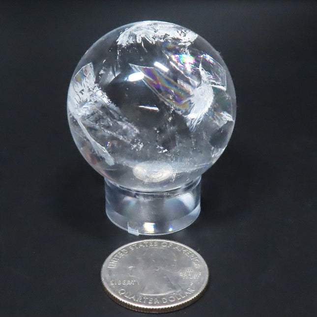 Clear crystal ball with rainbows from Brazil on a stand with a quarter for scale against a dark background