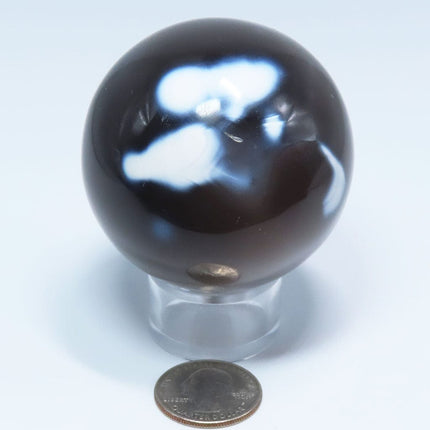 Polished Snow Blue Agate Sphere Ball from Madagascar on a stand with a quarter for scale on a light blue background