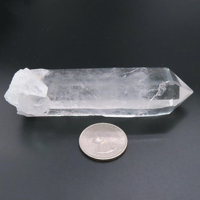 Arkansas Quartz Crystal Point with a coin for scale on a dark background