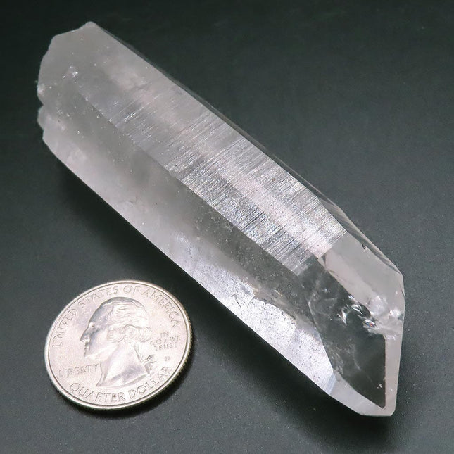 Arkansas Quartz Crystal Point next to a quarter dollar coin on a dark surface