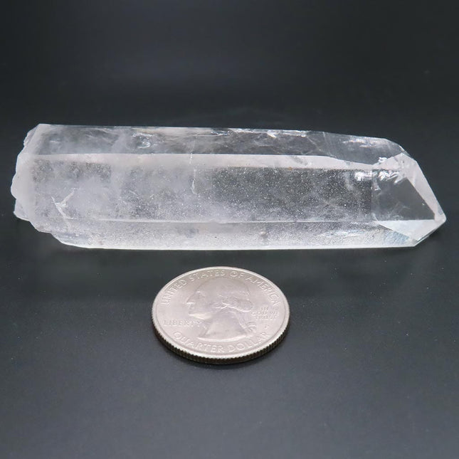 Arkansas quartz crystal point next to a U.S. quarter on a dark background