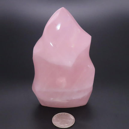 Polished Rose Quartz Flame Carving from Madagascar on a dark background with a coin for scale