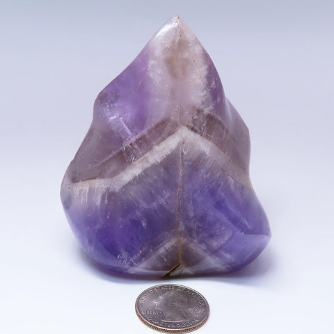 Polished Smoky Amethyst Flame Carving from Madagascar with a quarter for scale on a light gray background